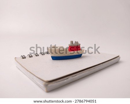 A tiny model ship with a red funnel sits centered on a closed white spiral notebook.