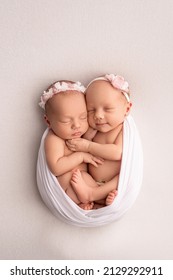 Tiny newborn twin girls. A newborn twin sleeps next to his sister Newborn twin girls on the background of a white blanket with pink bandages. The girls gently hug and kiss their sister in a cute pose - Shutterstock ID 2129292911