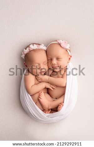 Tiny newborn twin girls. A newborn twin sleeps next to his sister Newborn twin girls on the background of a white blanket with pink bandages. The girls gently hug and kiss their sister in a cute pose