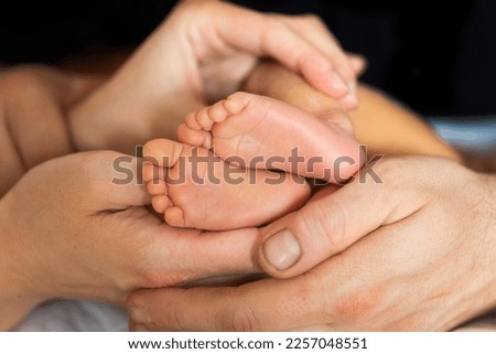 Tiny  newbornbaby's feet and toes in palms of new parents, mom and dad 