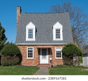 Tiny, red brick house with steep, gray roof and white dormers.