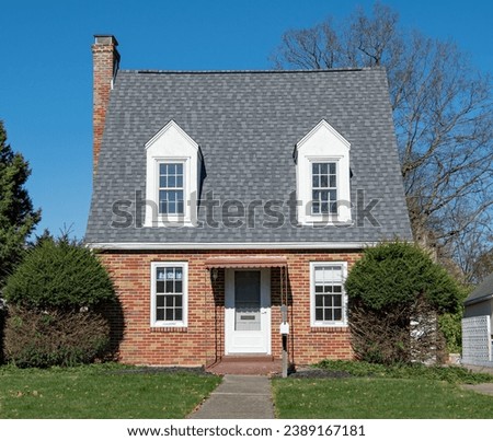 Tiny, red brick house with steep, gray roof and white dormers.