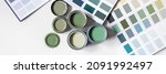Tiny sample paint cans during house renovation, process of choosing paint for the walls, different green colors, color charts on background, banner size