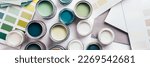 Tiny sample paint cans during house renovation, process of choosing paint for the walls, different green and beige colors, color charts on background, banner size