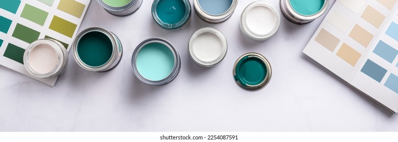 Tiny sample paint cans during house renovation, process of choosing paint for the walls, different blue, green and white colors, color charts on background, banner size