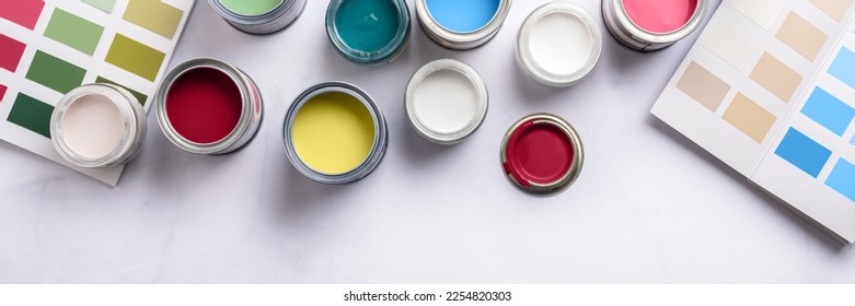 Tiny sample paint cans during house renovation, process of choosing paint for the walls, different colors, color charts on background, banner size
