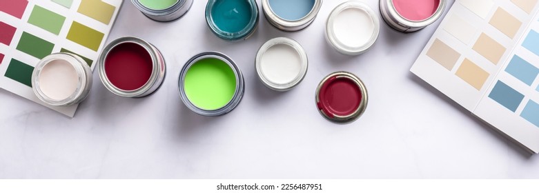 Tiny sample paint cans during house renovation, process of choosing paint for the walls, different colors, color charts on background, banner size