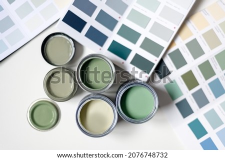 Tiny sample paint cans during house renovation, process of choosing paint for the walls, different green colors, color charts on background