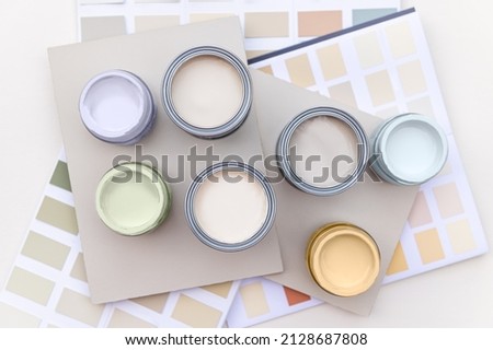 Tiny sample paint cans during house renovation, process of choosing paint for the walls, light grey and pastel colors, color charts and unit samples on background