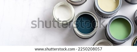 Tiny sample paint cans during house renovation, process of choosing paint for the walls, different green and beige colors, color charts on background