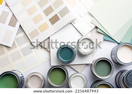 Tiny sample paint cans during house renovation, process of choosing paint for the walls, different green and beige colors, color charts on background