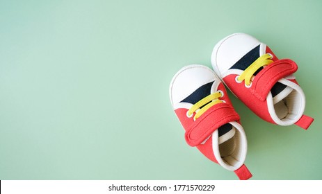 Tiny Sneakers On Green Background. Footwear For Infant Baby. Copy Space. Babyhood Concept