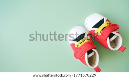 Tiny sneakers on green background. Footwear for infant baby. Copy space. Babyhood concept