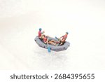 Tiny toy figures ride a small boat across an icy, snowy surface