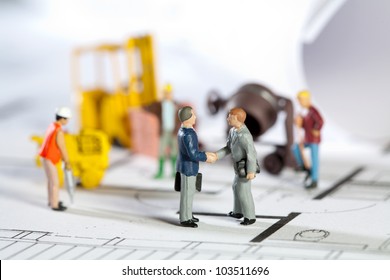 Tiny toy model figures of tradesmen and workers in the construction industry with their equipment on a building site on a blueprint plan for a house design
