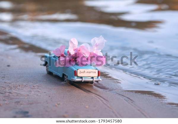 Tiny toy retro car\
full of pink flowers and wooden plate with text \