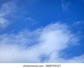 A tiny white airplane soars gracefully through a vast, brilliant blue sky, contrasting beautifully with soft, wispy clouds. The minimalist composition captures a profound sense of freedom, adventure, and boundless exploration, perfectly illustrating the peaceful majesty of high-altitude flight and the romantic allure of traveling to far-off horizons.