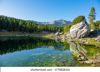 Tiny wooden cabin faces the tranquil lake in picturesque Triglav National Park. Spectacular shot of untouched nature surrounding a lake in the scenic Julian Alps. Gorgeous scenery near Seven Lakes.