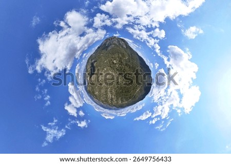 Tiny world of a landscape with clouds and blue sky. A captivating miniature world, or a small planet, perspective photo shows a landscape, possibly a forested area, nestled within a vibrant blue sky 