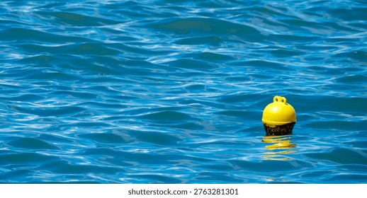 Tiny yellow spherical warning float positioned far out on the expansive textured surface of rich blue sea water offering guidance to incoming boats on a bright day