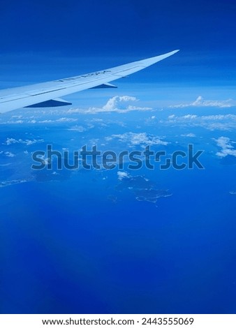 The tip of an airplane wing. The wing is metallic and has a smooth, aerodynamic shape.
Bright blue ocean, the water is clear and calm, with small whitecaps breaking the surface in the distance.
