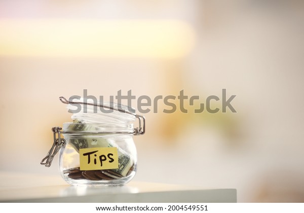 Tip jar with money on table against blurred\
background, space for text