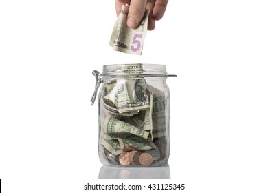 A Tip Or Savings Jar Filled With American Coins And Bills And Someone About To Add A Five Dollar Bill.