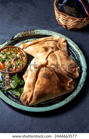 Tipical baked empanadas de pino with pebre sauce on vintage try, black stone background. Traditional chilean food for independence day party