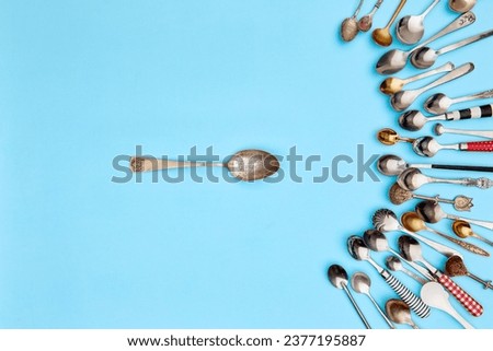 Tips of cutlery. Top view photo one table spoon surrounded of variety of antique silverware and gold spoons against blue studio background. Concept of food, holiday, table setting, retro, vintage