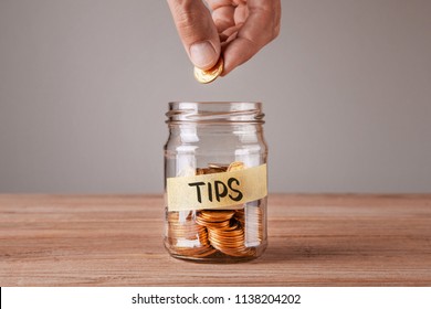 Tips. Glass jar with coins and an inscription tips. Man holds  coin in his hand