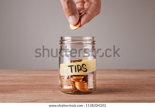 Tips. Glass jar with coins and an inscription\
tips. Man holds  coin in his\
hand
