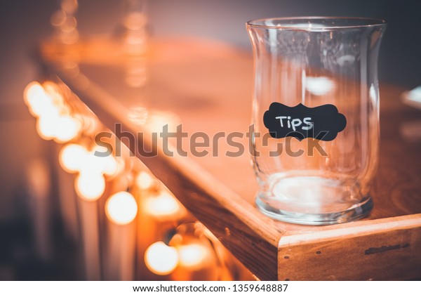 Tips Jar on a bar\
countertop. Bokeh lights along a bar counter with a tip Jar at the\
end. Gold Bokeh lights.