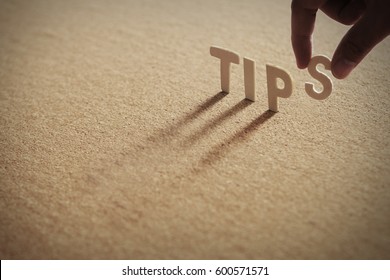 TIPS wood word on compressed or corkboard with human's finger at S letter.