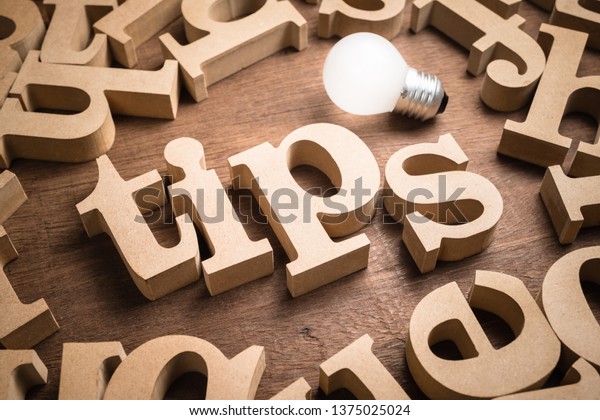Tips wood word in scattered wood letters with\
glowing light bulb