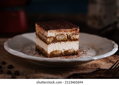 Tiramisu cake dessert served with coffee, biscuit and cocoa as ingredients in moody, dark background. One piece