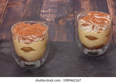 Tiramisu In A Glass Container Against A Dark Wood Countertop