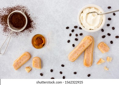 Tiramisu ingredients, ladyfingers, mascarpone, cocoa, almond liqueur and scattered black coffee beans on gray textured background with copy space. Top view.