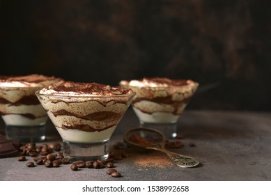 Tiramisu - traditional italian dessert from mascarpone cheese and biscuit in a glasses on a dark slate, stone or concrete background. No baked chessecake.