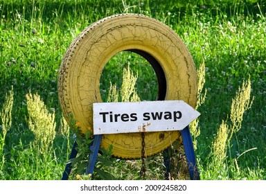 Tire With Arrow-shaped Information Plate With The Inscription Tires Swap, In The Background Of The Lawn In Summer