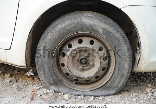 Tire leak, close up wheel\
of old white vintage car. Car wheel flat tire on the road. Deflated\
the tyre of an old car next to a motorcycle. - Udaipur India :\
February 2020