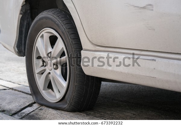 Tire leaks flat on the ground. Dirty white car Flat\
wheel with road