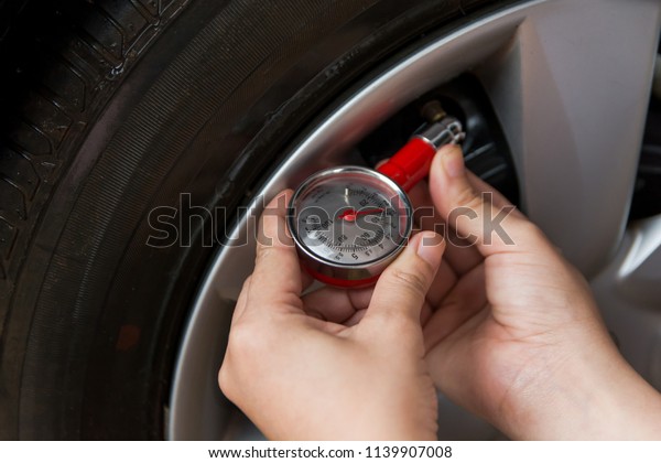 Tire pressure gauge : Hand\
holding pressure gauge checking air pressure for car tire. Safe\
driving.