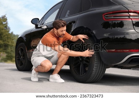 Tire puncture. Man checking wheel of car on roadside outdoors