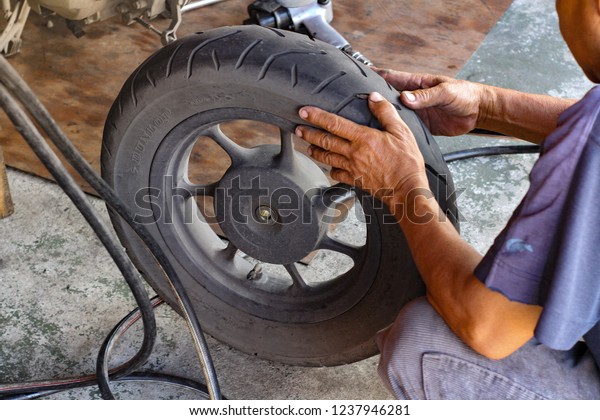 Tire repairing, Motorcycle tire check with\
technician man hand close up Holding equipment tools Transportation\
maintenance Bangko Thailand 18 November 2018, natural day low light\
tone with copy space