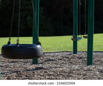 A Tire Swing And Two Empty Swings On A Green Playground.