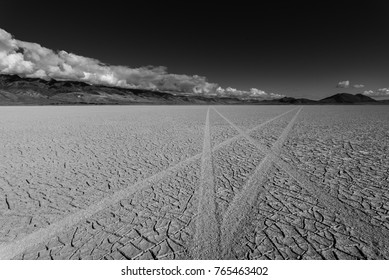 Tire tracks cross on dry lake bed. Black and white photo