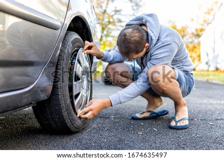 Tire wheel with missing cap cover on parked car with man replacing hubcap with new shiny metal outside