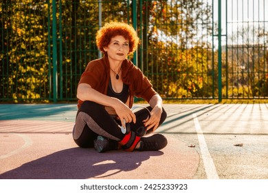 Tired adult woman in sportswear sitting crossed legs on playground. Concept of healthy lifestyle and sport. - Powered by Shutterstock