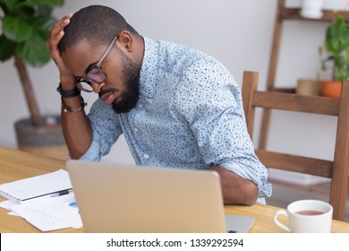 Tired African American businessman sitting at desk falling asleep, overworked, sleepy lazy employee or student disinterested in boring routine job, dozing on hand during break, insomnia concept
