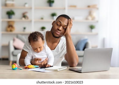 Tired African American Father With Infant Baby Working On Laptop At Home Office, Exhausted Black Freelancer Man Sitting At Desk With Computer And Holding Little Child, Having Multitasking Stress